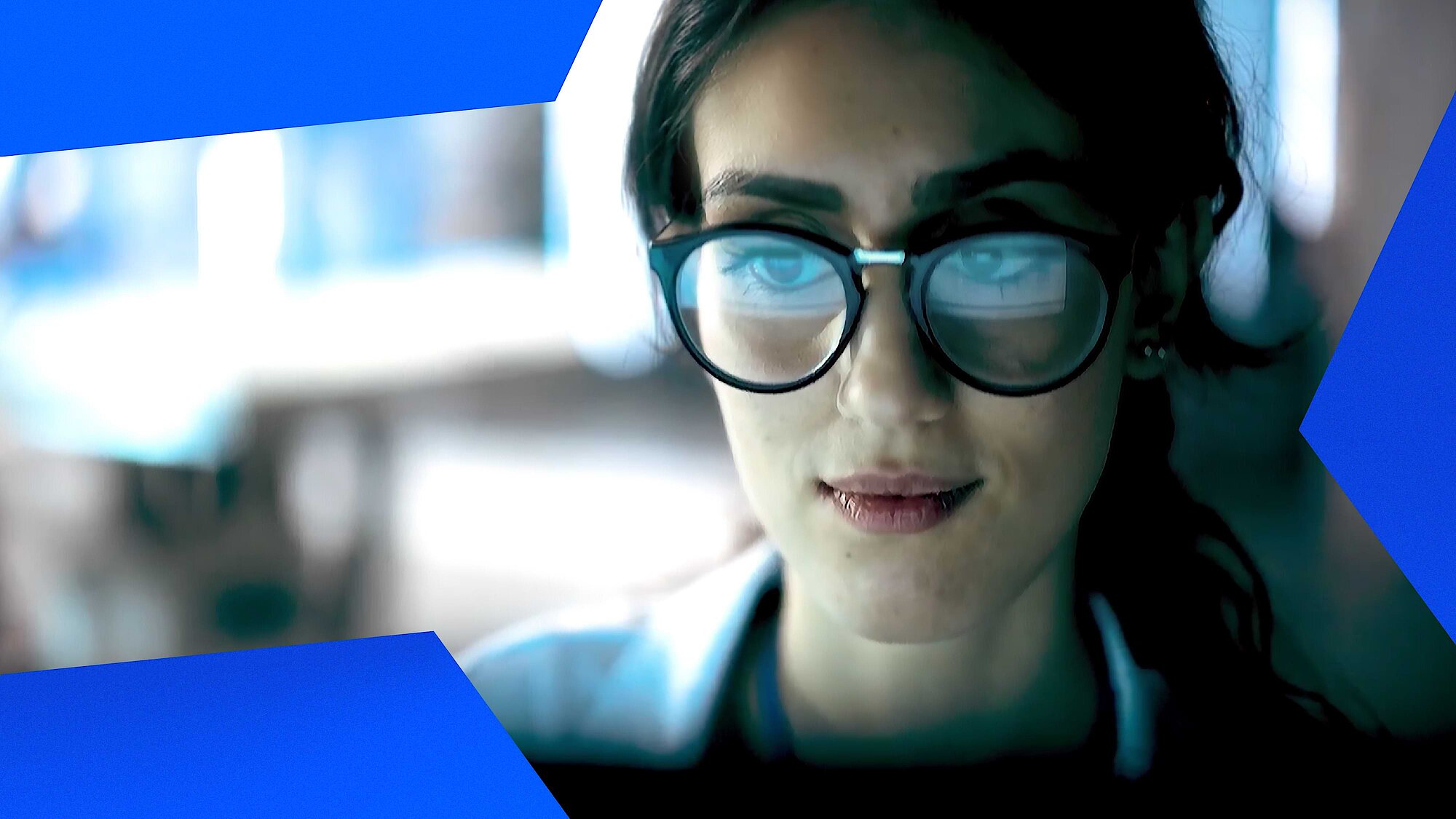 Showing a portrait of a woman with glases looking at a computer screen.