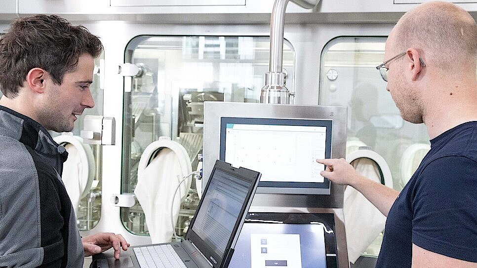 Shows two people in a pharmaceutical production facility in front of a pharmaceutical isolator from Körber.